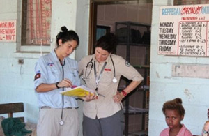 Two medical volunteers consulting notes outside a small clinic. 