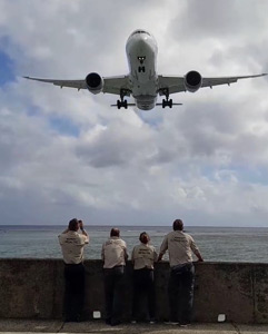 A group of volunteers by the sea watching a plane come in to land. 