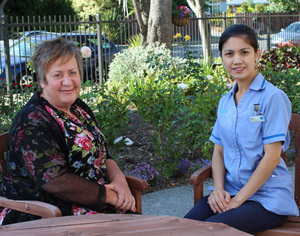 One older and one younger nurse sitting outside in a garden. 