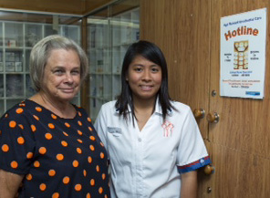Two nurses standing together next to a telephone hotline poster. 