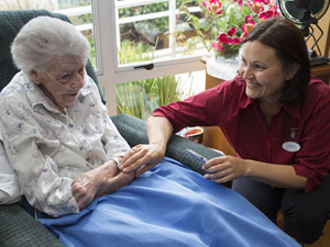 A smiling nurse crouching down to talk with a frail-looking older woman. 