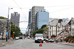 Photo of a cordoned-off street. Most of the buildings are standing, but one has collapsed.
