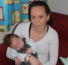 Photo of a young woman, holding a sleeping baby and looking quite tired herself. 