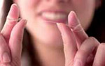 Photo of a young woman about to floss her teeth. She has the floss wrapped around her forefingers and supported on her thumbs, with about 10 cm of floss free between her fingers. 