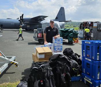 An NZMAT volunteer standing with unloaded supplies on the airfield in Vanuatu.