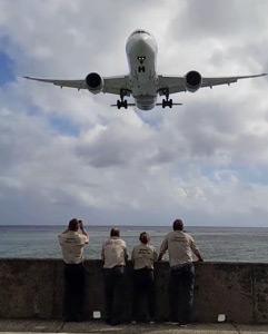 A group of volunteers by the sea watching a plane come in to land.
